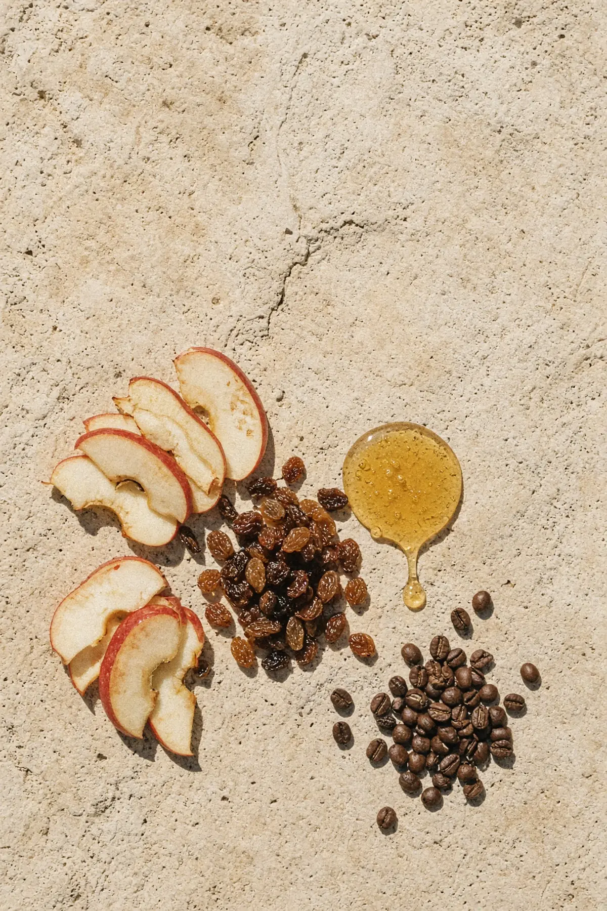Apple slices, raisins and honey beside coffee beans on stone